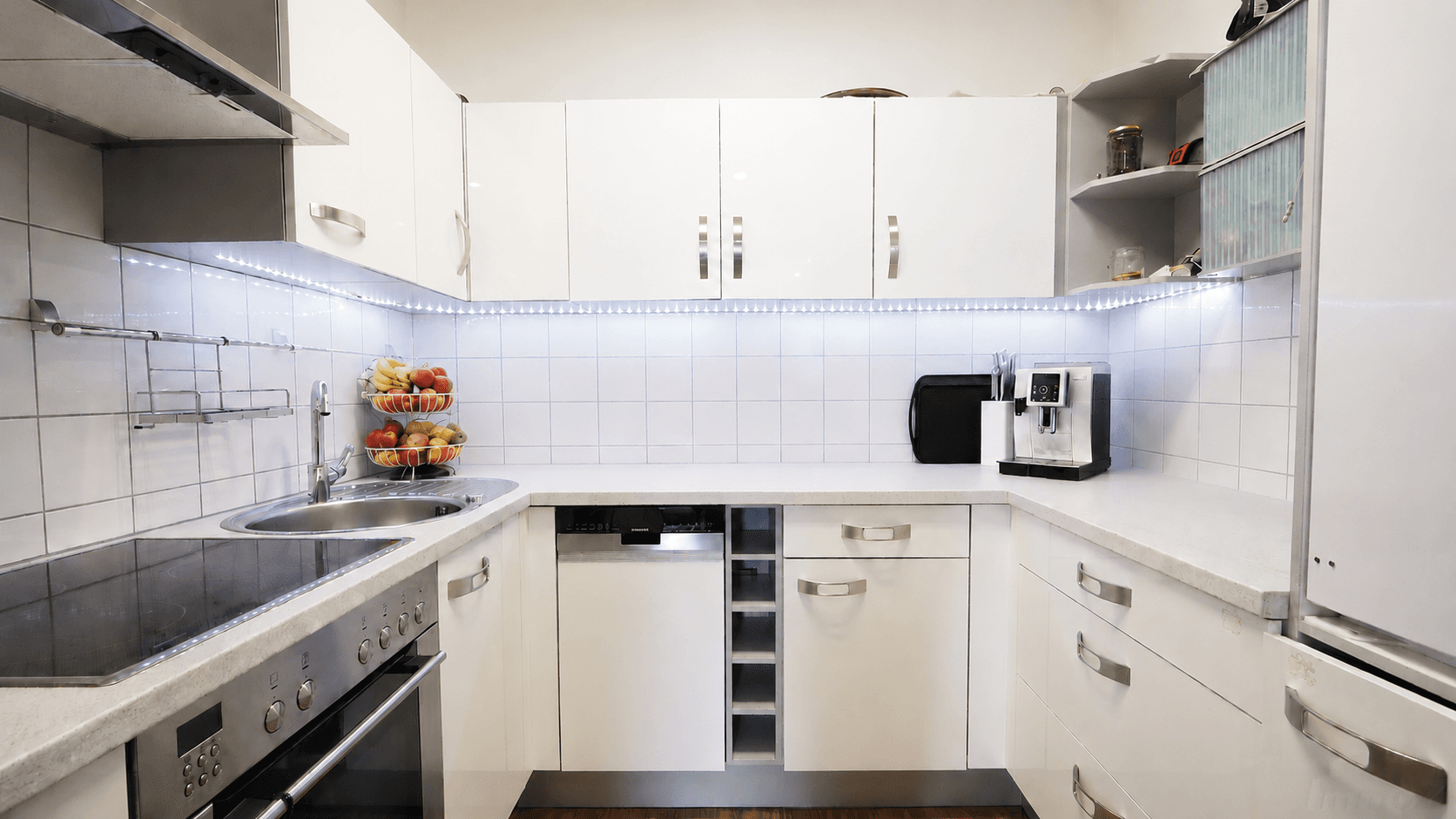 Moderne weiße Küche mit Hochglanzfronten, Einbaugeräten und LED-Beleuchtung unter den Schränken.