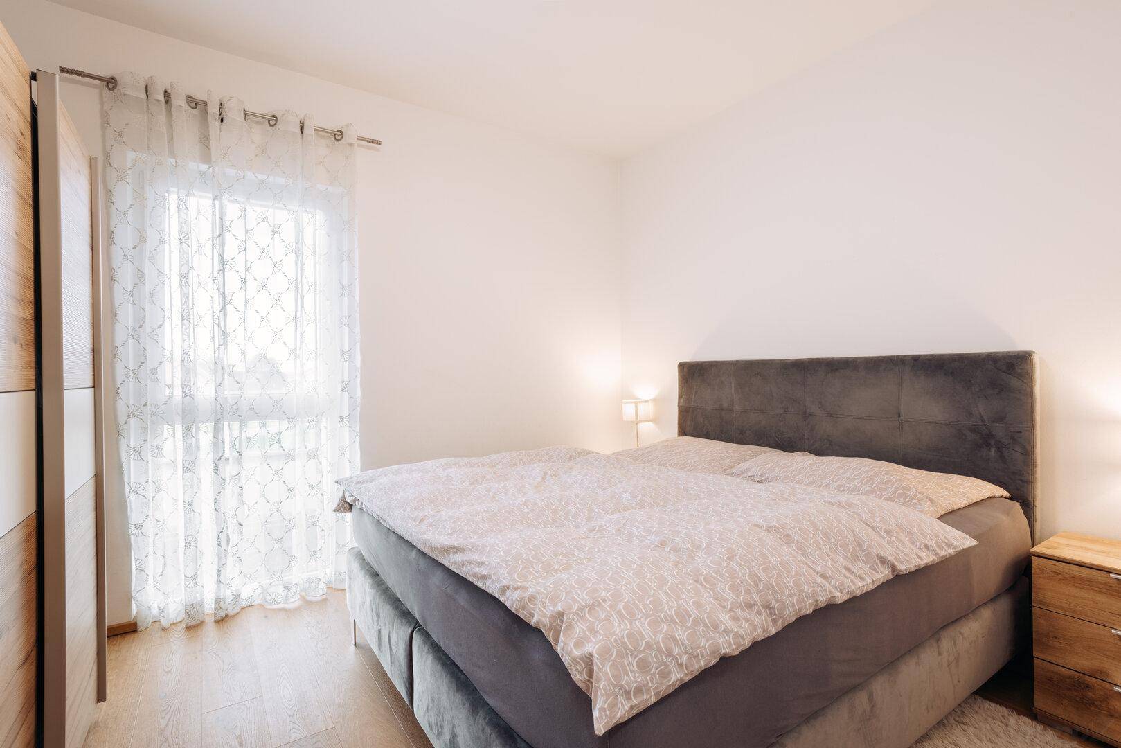 Helles Schlafzimmer mit Doppelbett, Holzboden und Fenster mit Blick ins Grüne.