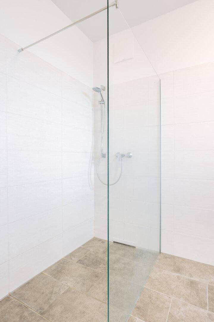 Geräumige, ebenerdige Dusche mit Glasabtrennung und modernen Fliesen.