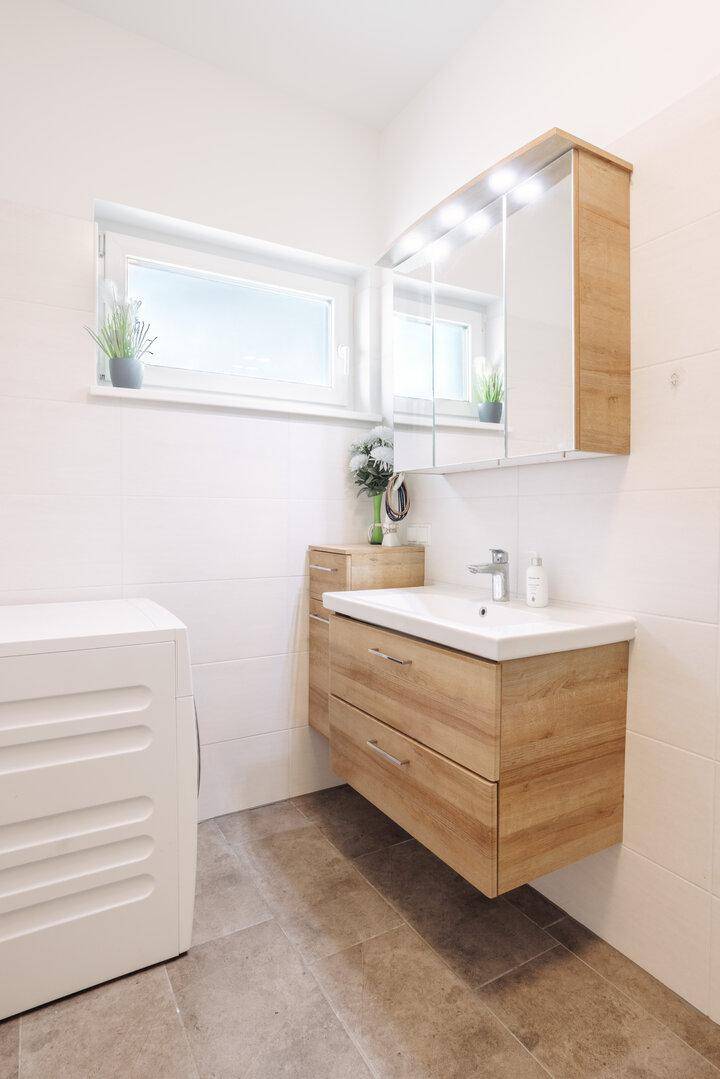Modernes Badezimmer mit Holzwaschtisch, Spiegelschrank und integrierter Waschmaschine.