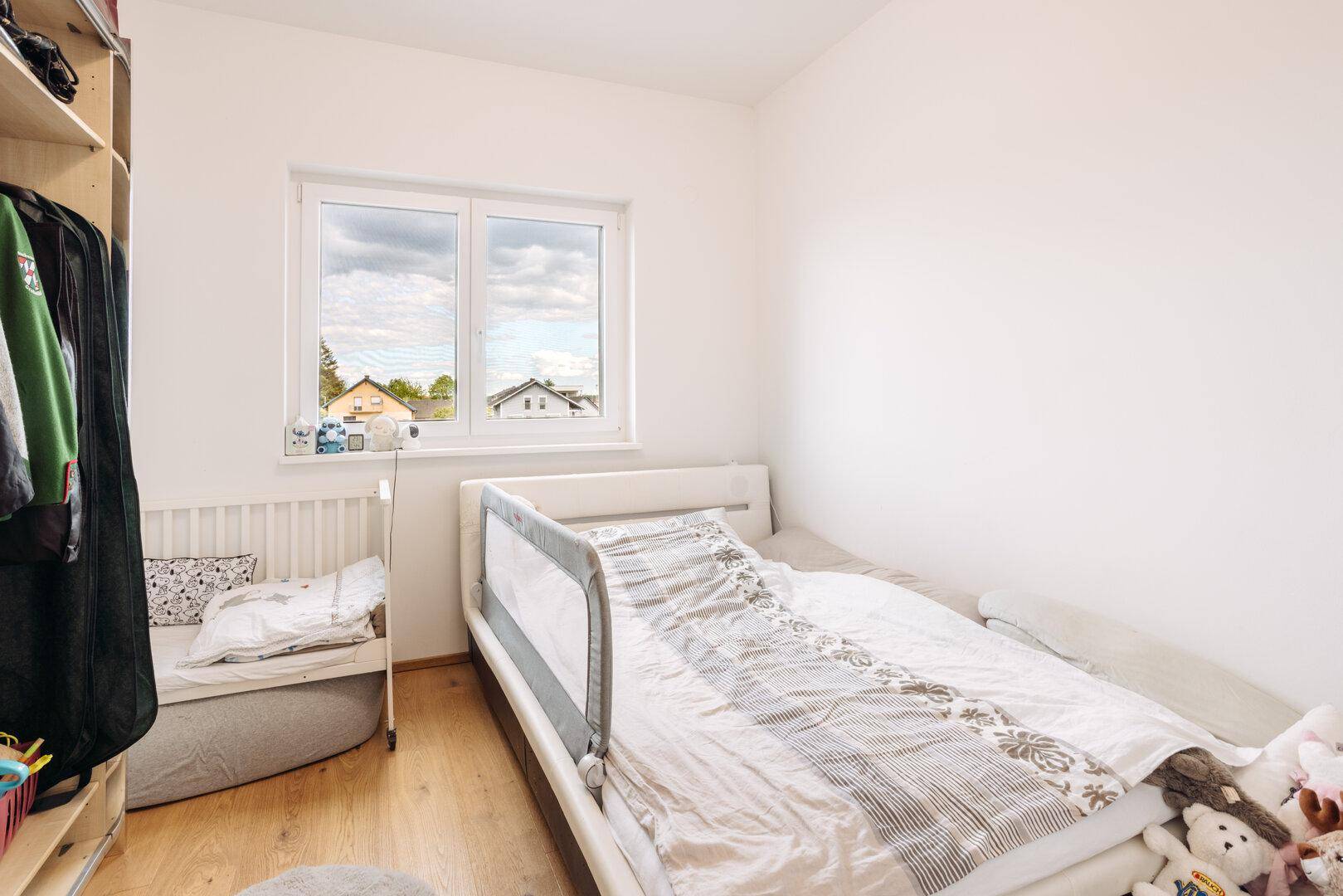Kinderzimmer mit Einzelbett, Babybett und Fenster, das viel Tageslicht hereinlässt.