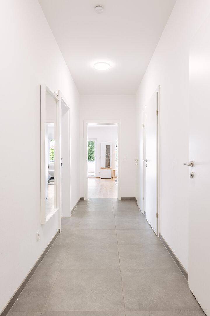 Heller Flur mit Fliesenboden, weißen Wänden und Zugang zu verschiedenen Räumen.