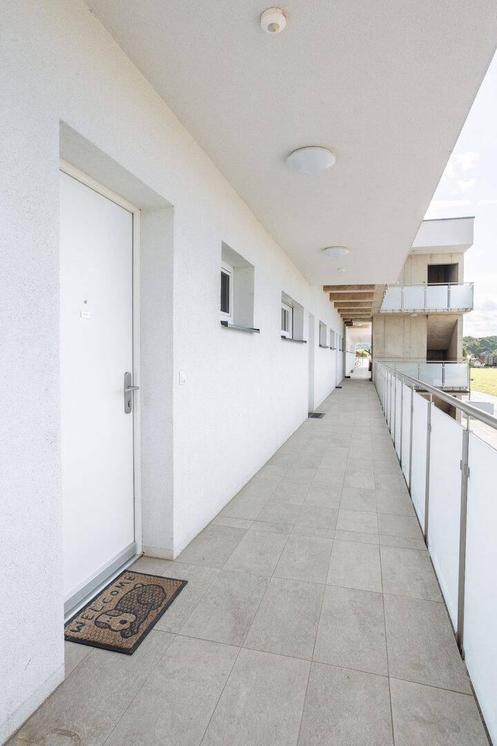 Überdachter Außenflur mit Fliesenboden, der zu den Wohnungseingängen führt.