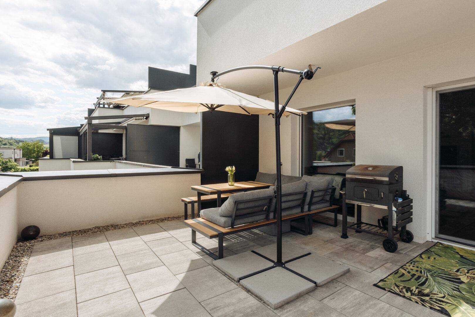 Geräumige Terrasse mit Essbereich, Sonnenschirm und Grill für entspannte Stunden im Freien.