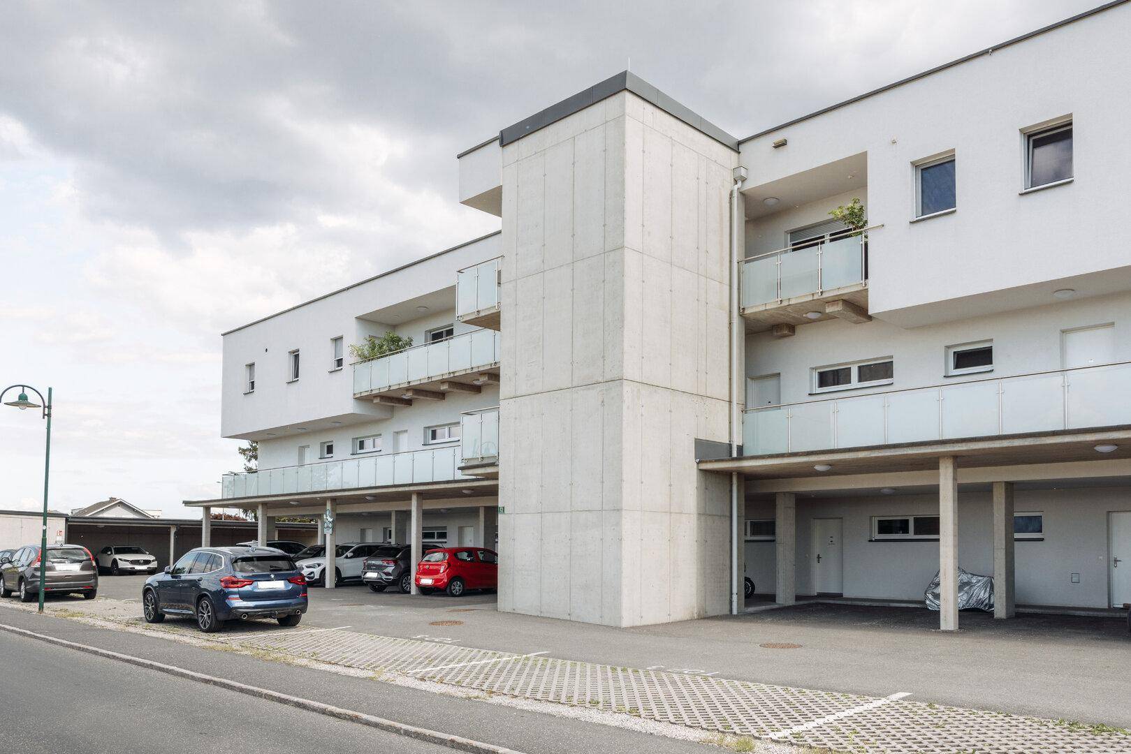 Modernes Mehrfamilienhaus mit Balkonen und überdachten Parkplätzen im Freien.