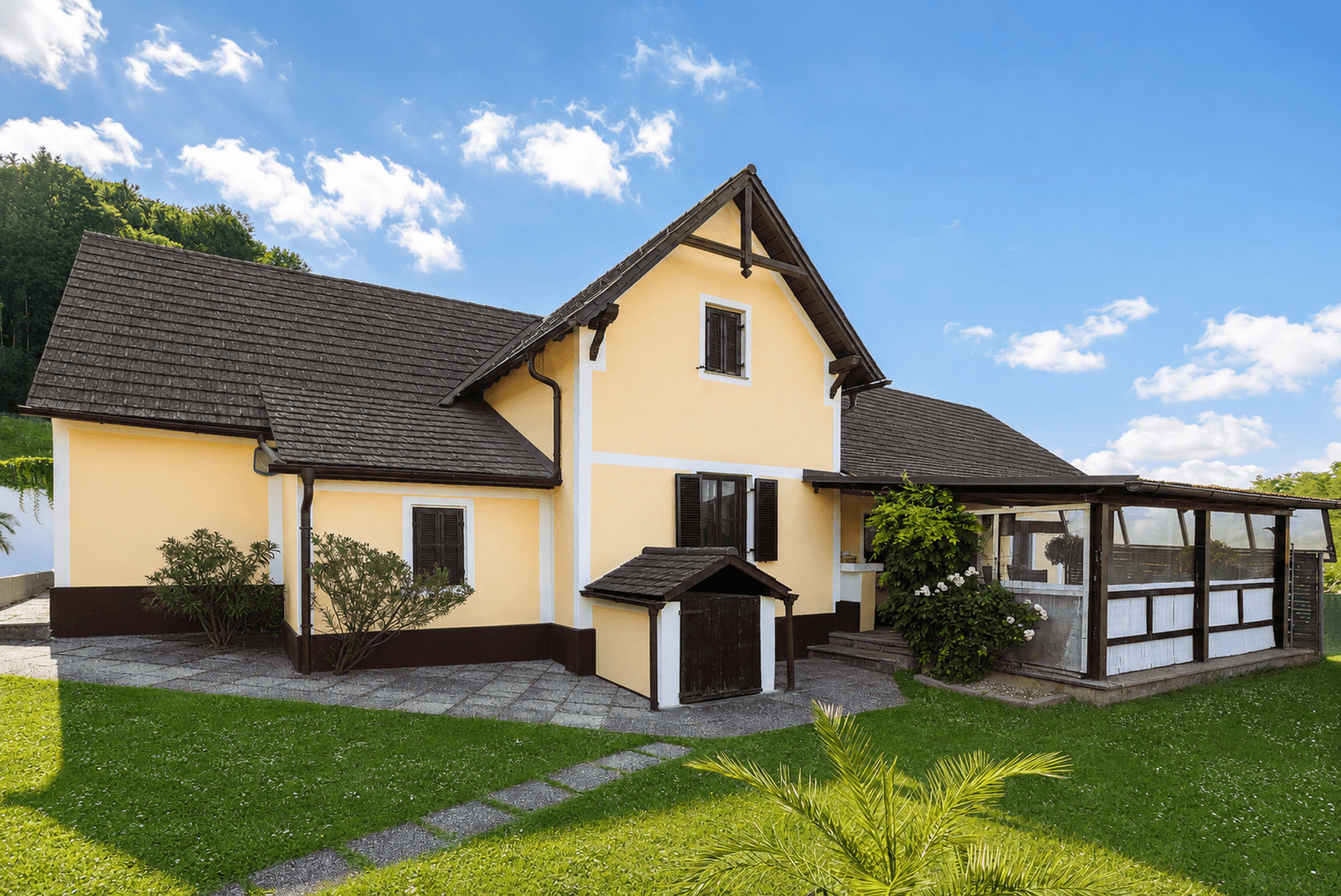 Traditionelles Landhaus mit gelber Fassade, braunem Dach und gepflegtem Vorgarten.