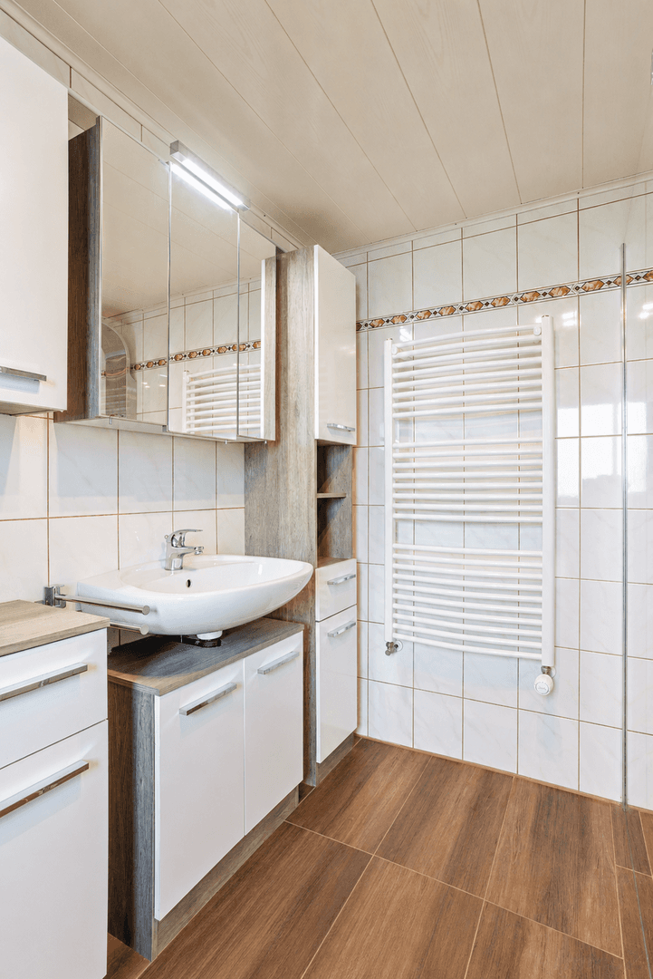 Modernisiertes Badezimmer mit Holzoptik-Fliesen, Waschbecken und beheiztem Handtuchhalter.