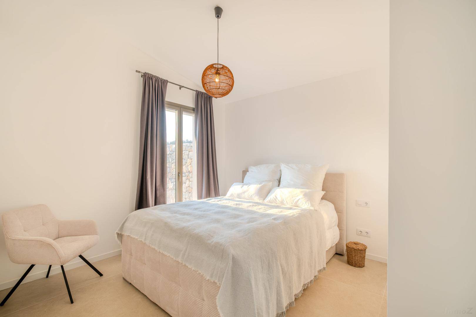 Freundliches Schlafzimmer mit Doppelbett, bequemen Sessel und großem Fenster für viel Tageslicht.
