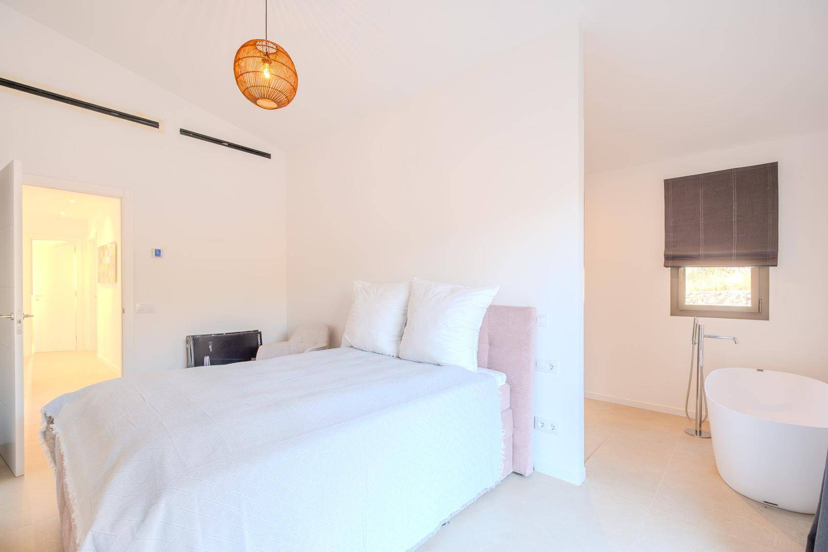 Helles Schlafzimmer mit Doppelbett, freistehender Badewanne und natürlichem Lichteinfall.