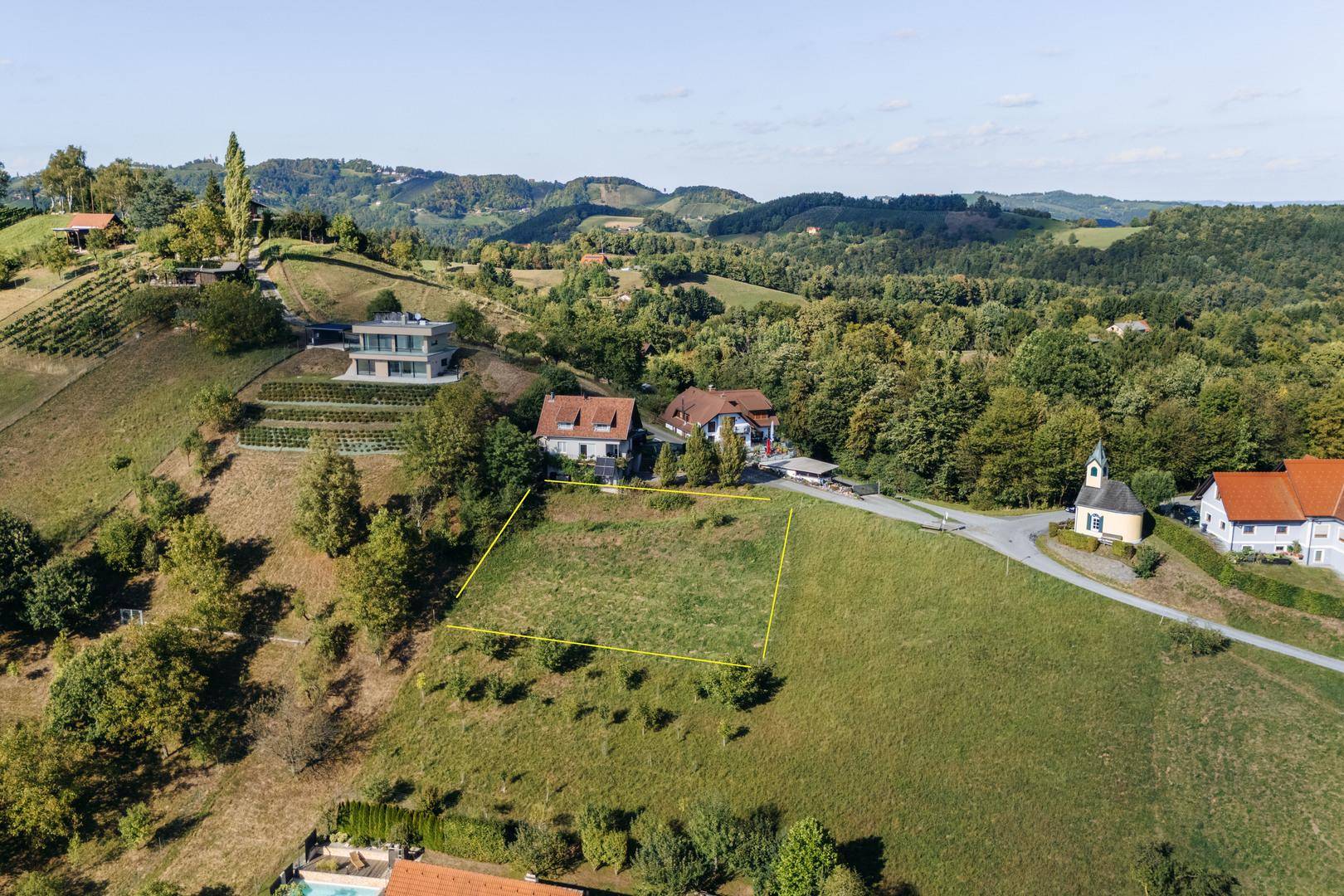 Luftaufnahme eines Baugrundstücks in Hanglage, umgeben von Weinbergen und Wohnhäusern mit moderner Architektur.