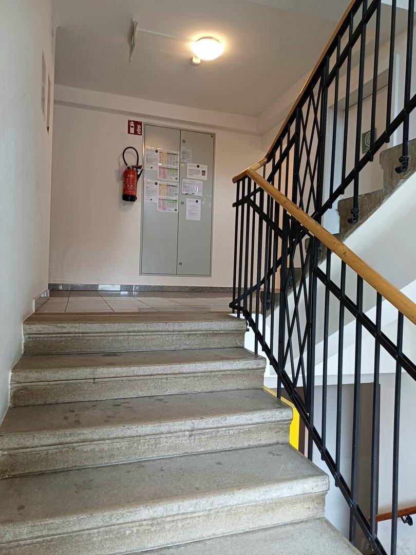 Treppenhaus mit Steinstufen, schmiedeeisernem Geländer und einem Feuerlöscher an der Wand.