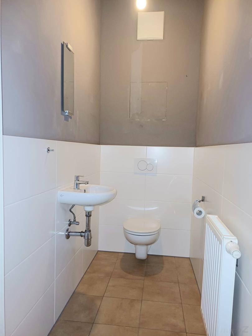Kleines Gäste-WC mit Toilette, Waschbecken, Heizkörper und zweifarbigen Fliesen an den Wänden.