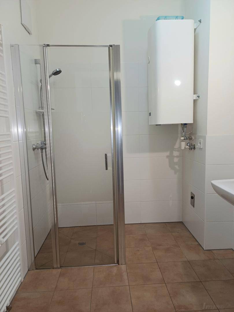 Modernes Badezimmer mit Duschkabine, weißen Fliesen, braunem Boden und einem beheizten Handtuchhalter.