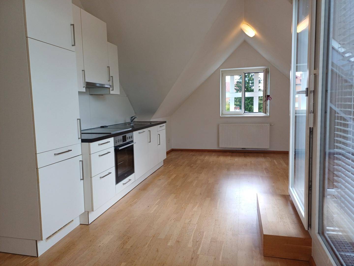 Offene Küche mit weißen Schränken und Holzboden in einem hellen Dachgeschosszimmer mit Zugang zur Terrasse.