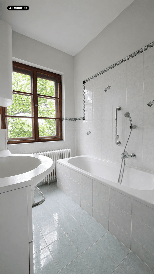 Helles Badezimmer mit Badewanne, Waschbecken und Fenster mit Blick ins Grüne.