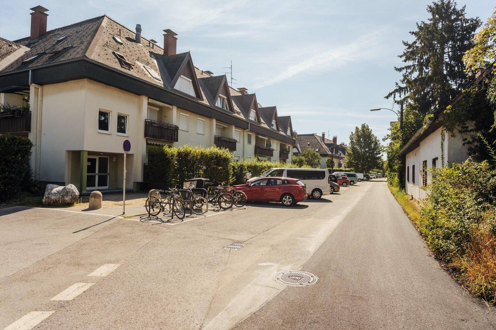 Ruhige Wohnstraße mit geparkten Autos und Mehrfamilienhäusern im Grünen.