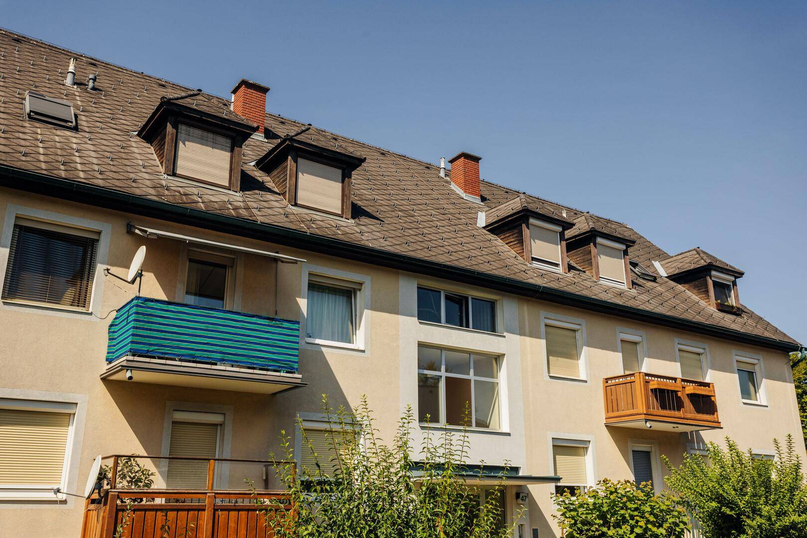 Mehrfamilienhaus mit Satteldach, Balkonen und Dachgauben in einer Wohnsiedlung.