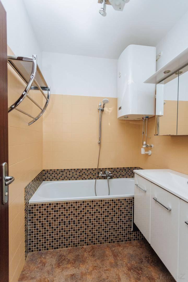 Badezimmer mit Badewanne, Waschtisch und Spiegelschrank, in neutralen Farben gehalten.