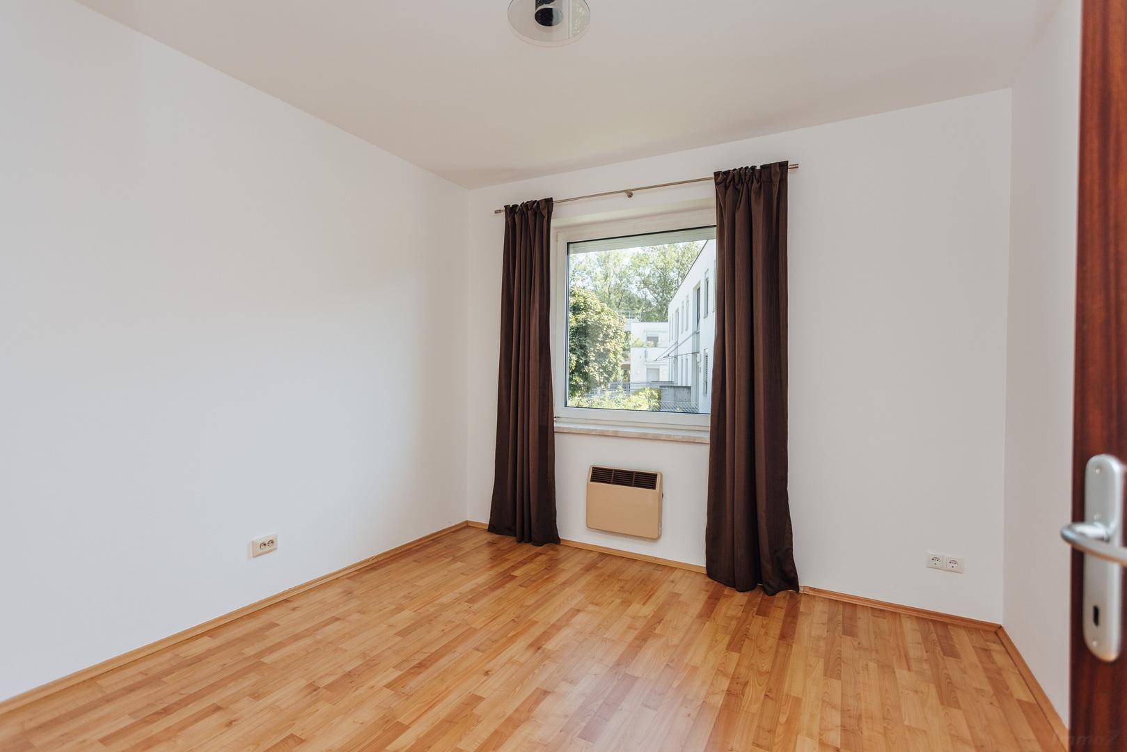 Leeres Schlafzimmer mit Holzboden und Fenster, das viel Tageslicht hereinlässt.