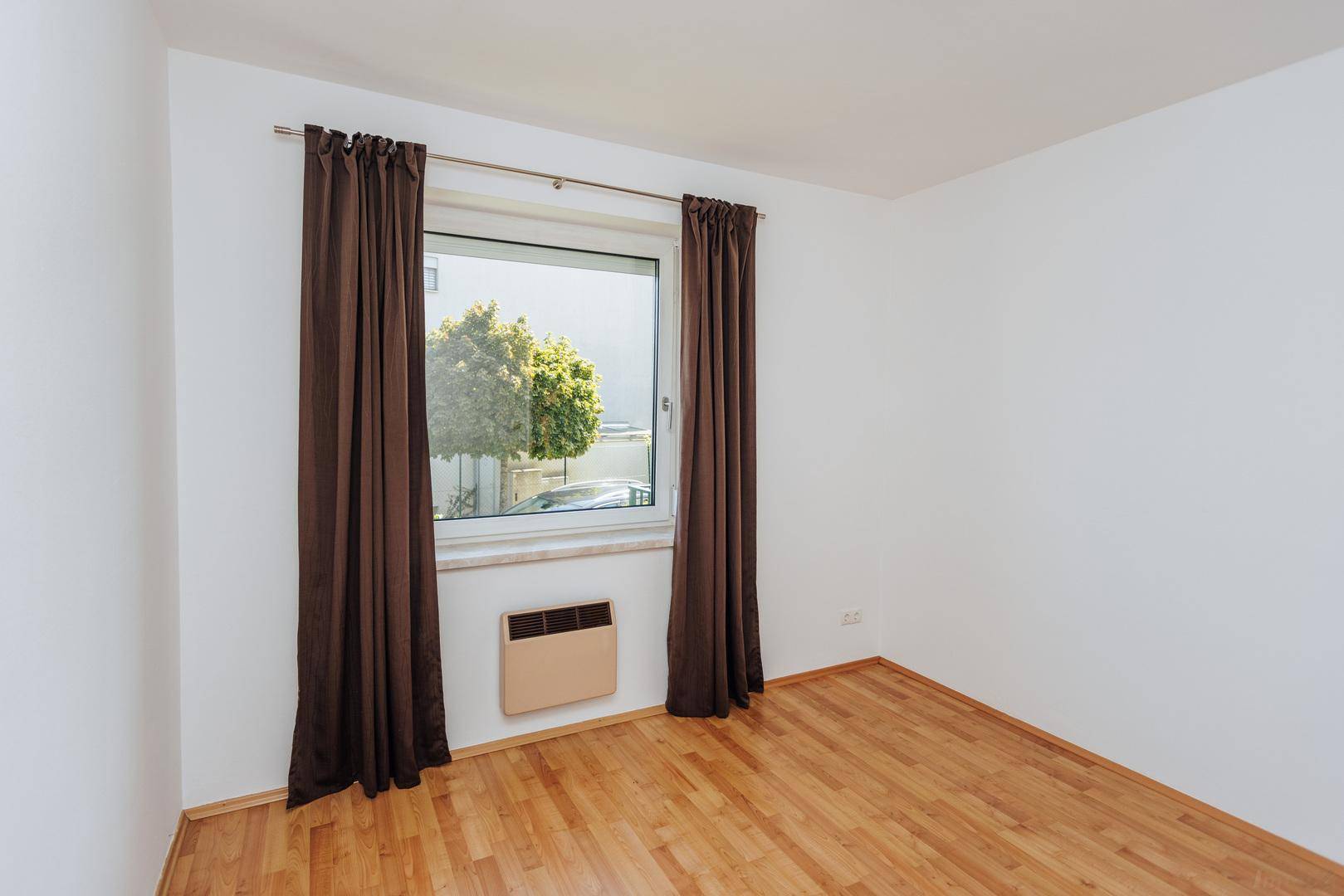 Helles, leeres Schlafzimmer mit Holzboden und Fenster mit Blick nach draußen.