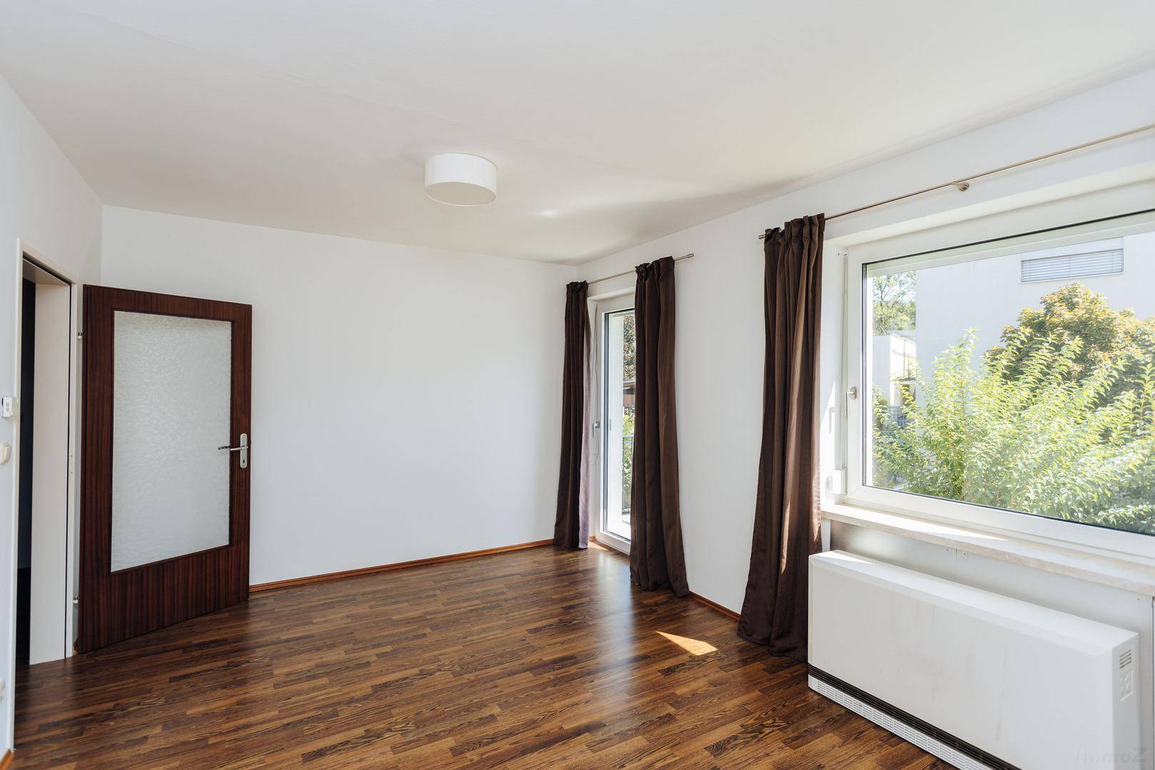 Helles, leeres Zimmer mit Holzboden und Balkonzugang, bereit zur Einrichtung.