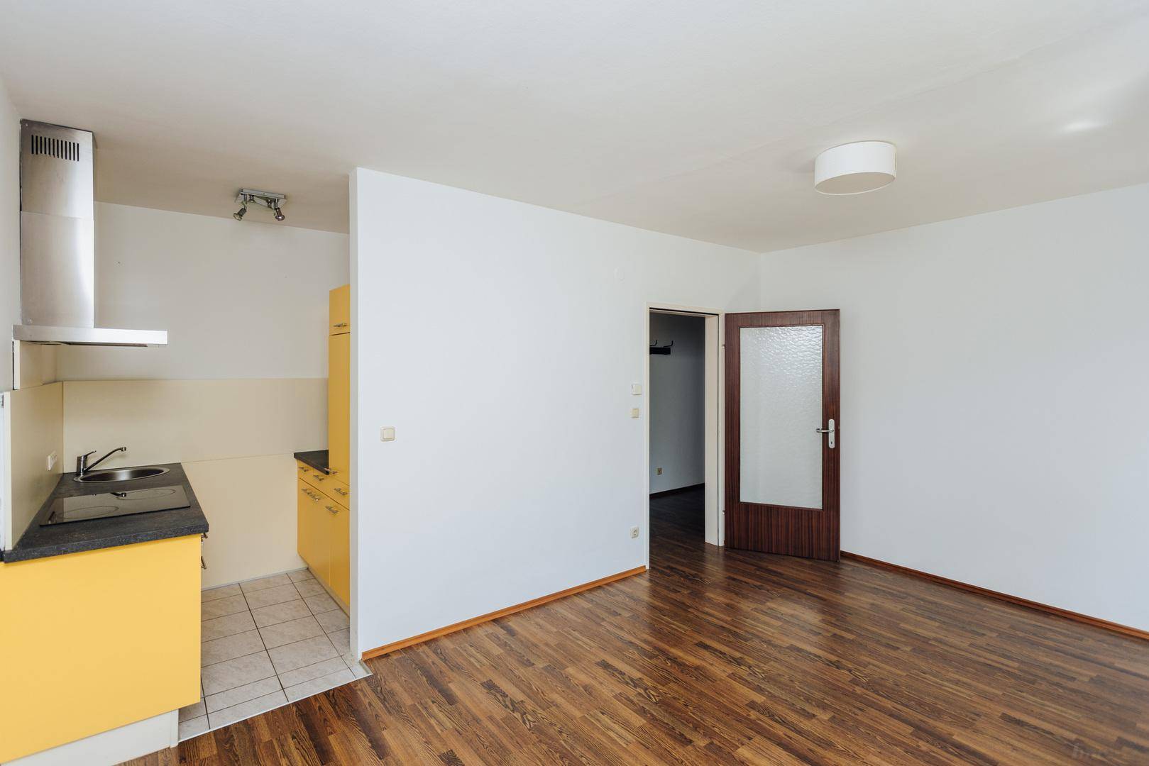 Leerer Wohnbereich mit offener Küche, Holzboden und weiß gestrichenen Wänden.
