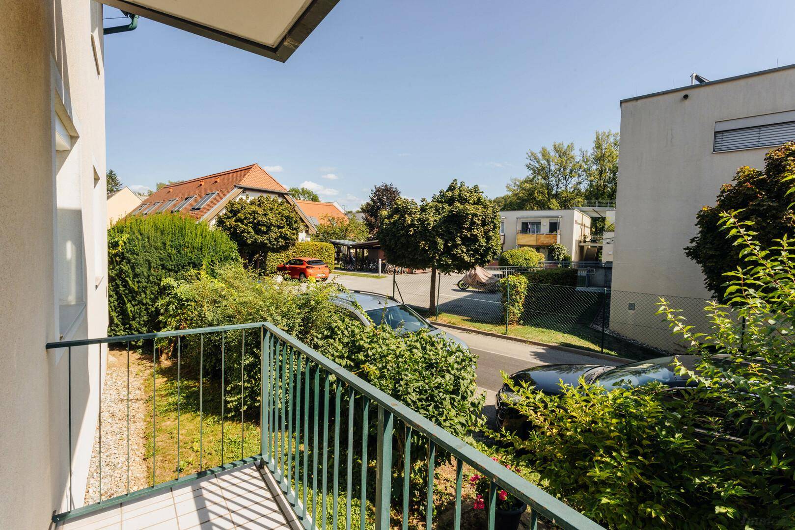 Balkon mit Ausblick auf die ruhige Wohnstraße und die grünen Büsche.