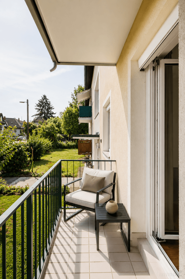 Gemütlicher Balkon mit Sitzgelegenheit und Blick ins Grüne an einem sonnigen Tag.