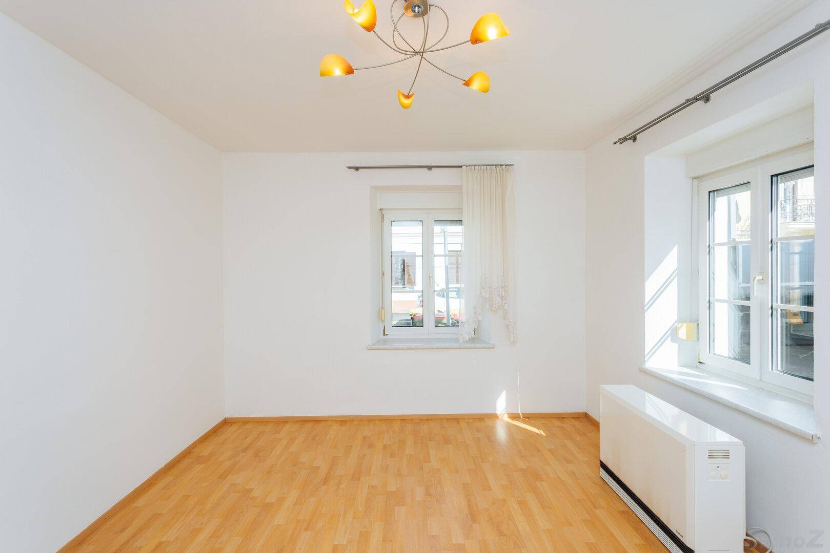 Leerer Raum mit hellem Holzboden, weißen Wänden und zwei Fenstern für viel Tageslicht.
