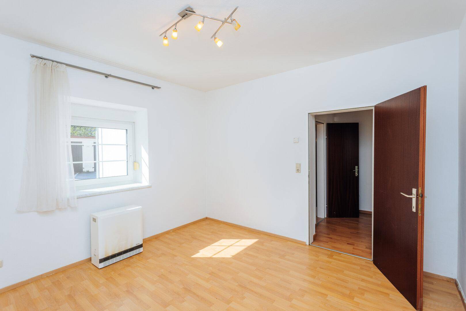 Leerer Raum mit Holzboden, einem Fenster und offener Tür, bereit zur individuellen Gestaltung.