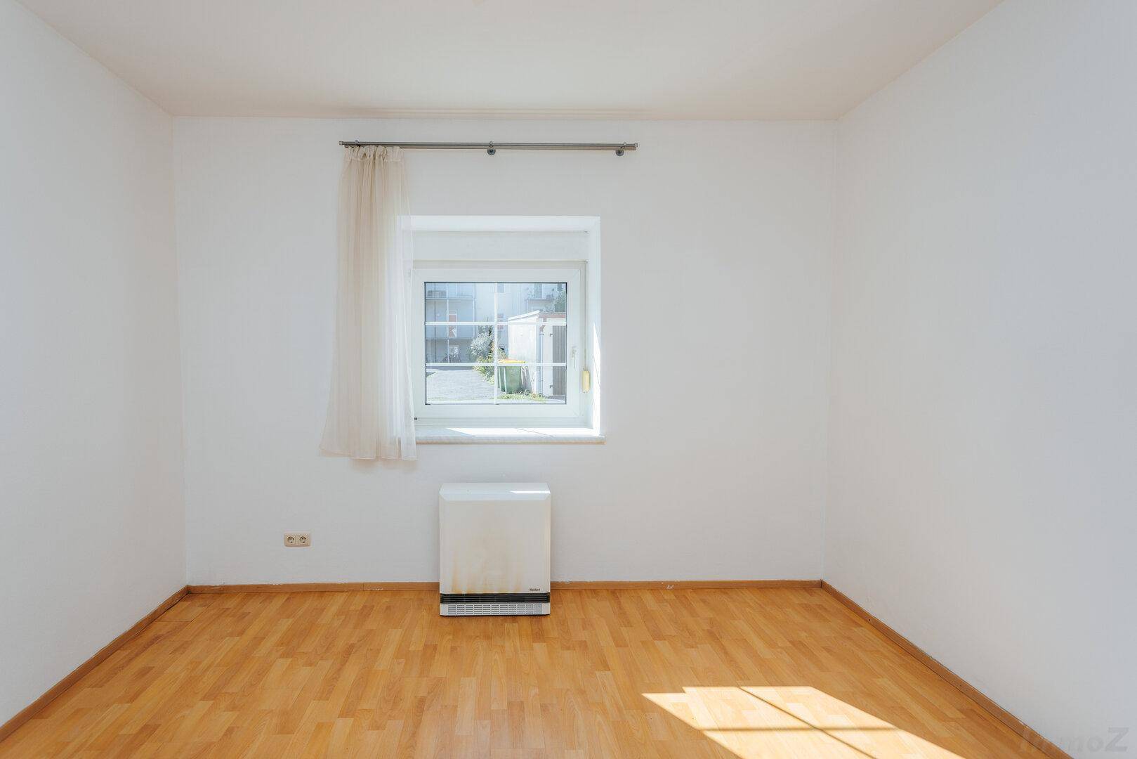 Heller, leerer Raum mit Holzboden und einem Fenster, das für natürliche Belichtung sorgt.