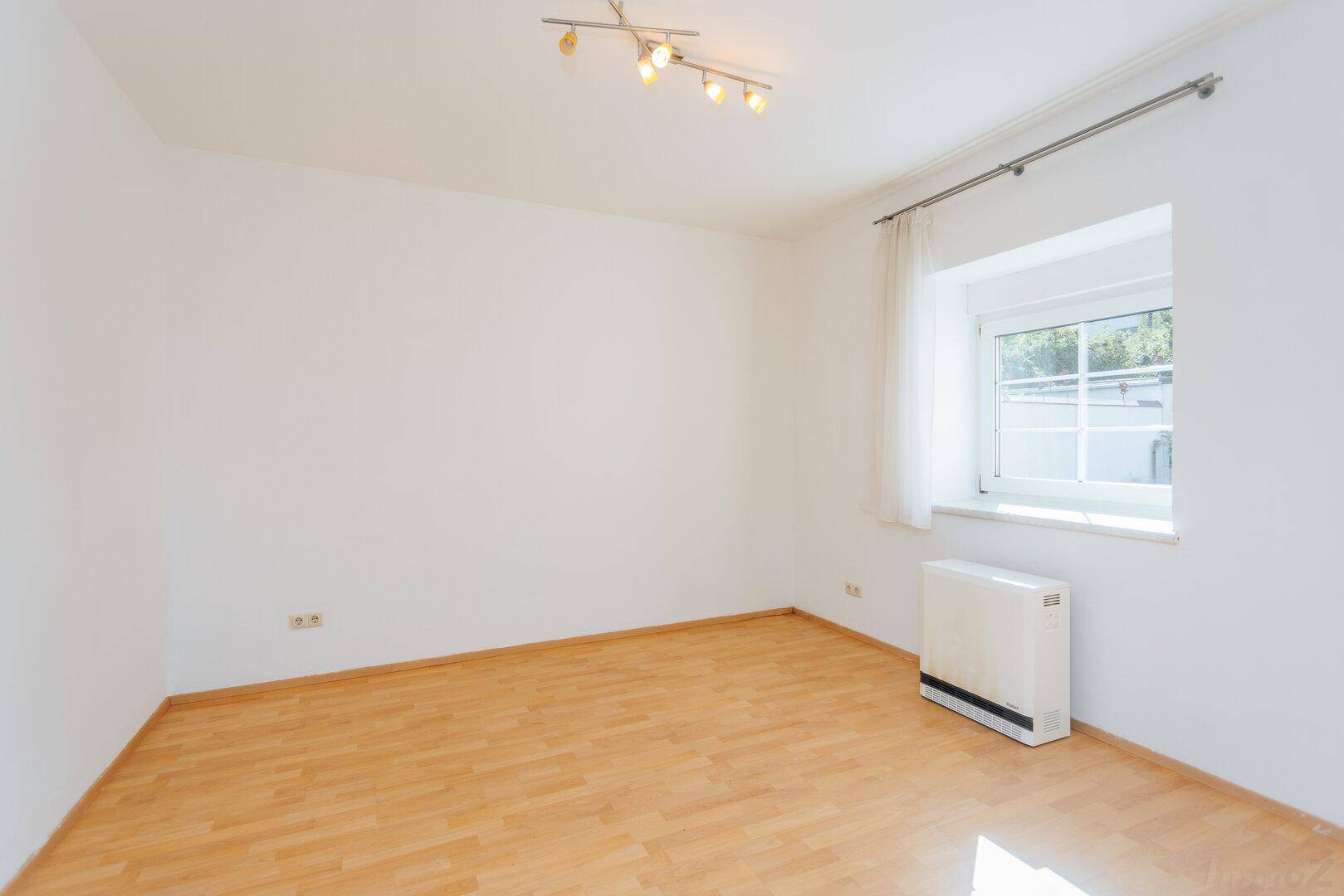 Heller, leerer Raum mit Holzboden und einem Fenster, das für natürliche Belichtung sorgt.
