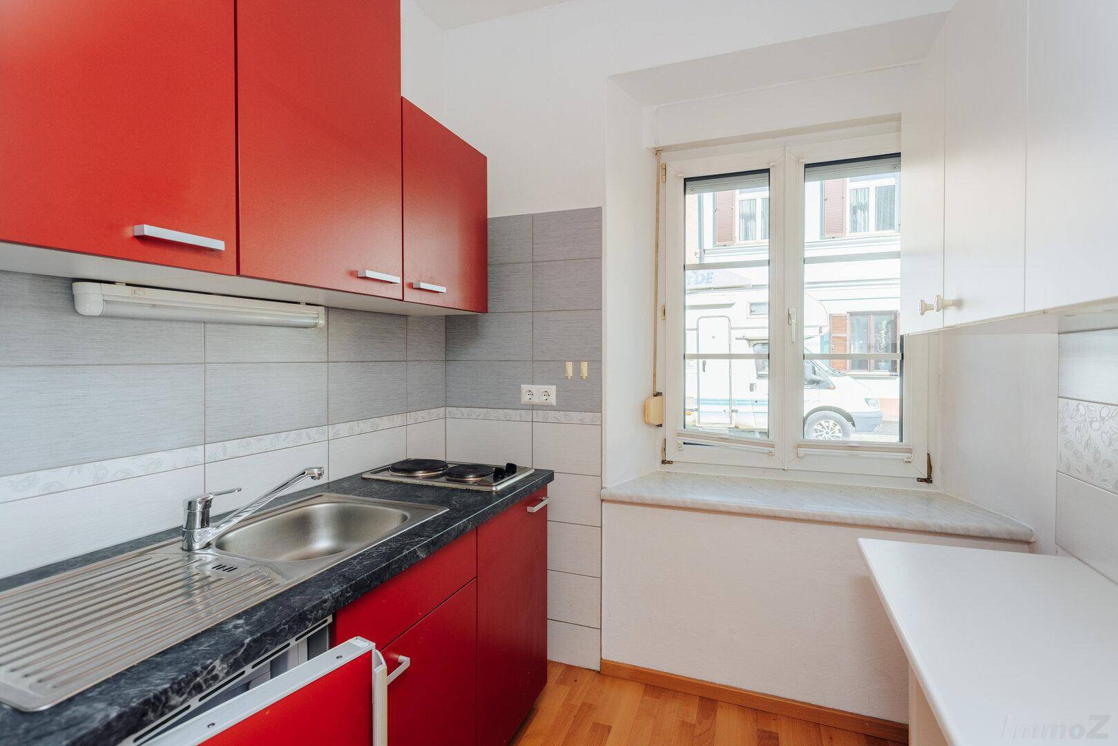 Funktionale Küche mit roten Schränken, Spüle und einem Fenster mit Blick nach draußen.