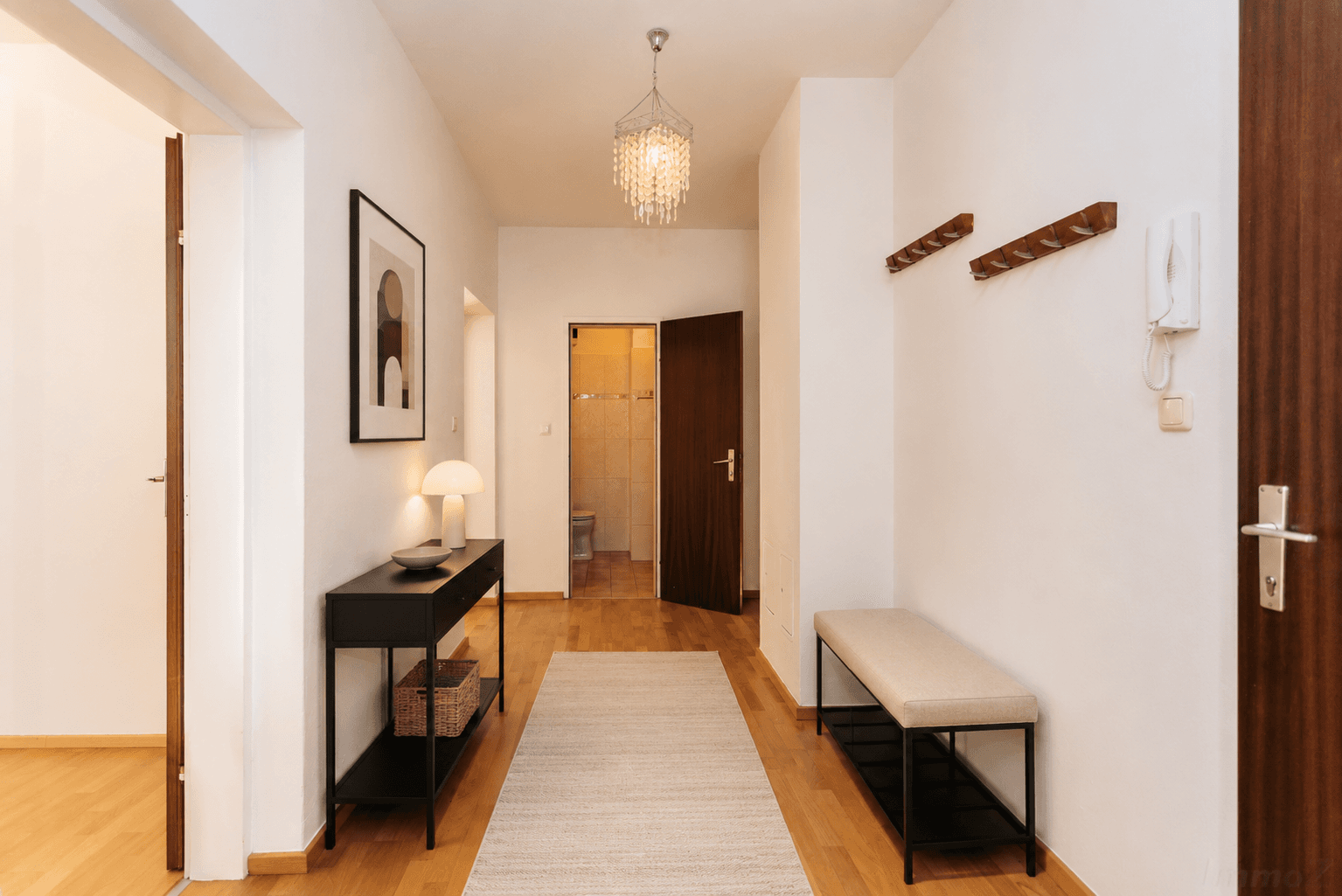 Heller Flur mit Holzboden, einer Konsole, Sitzbank und Blick in ein Badezimmer.