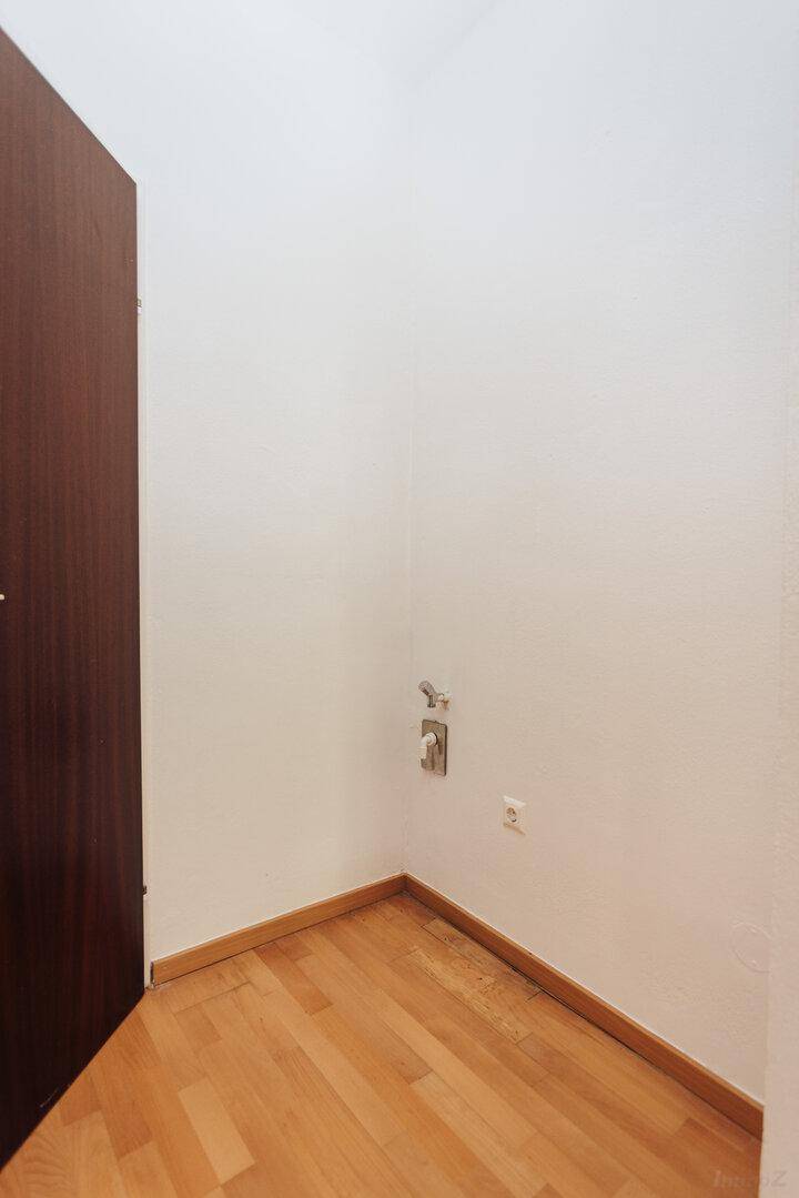 Leere Ecke eines Raumes mit Holzboden und Anschlüssen für eine Waschmaschine.