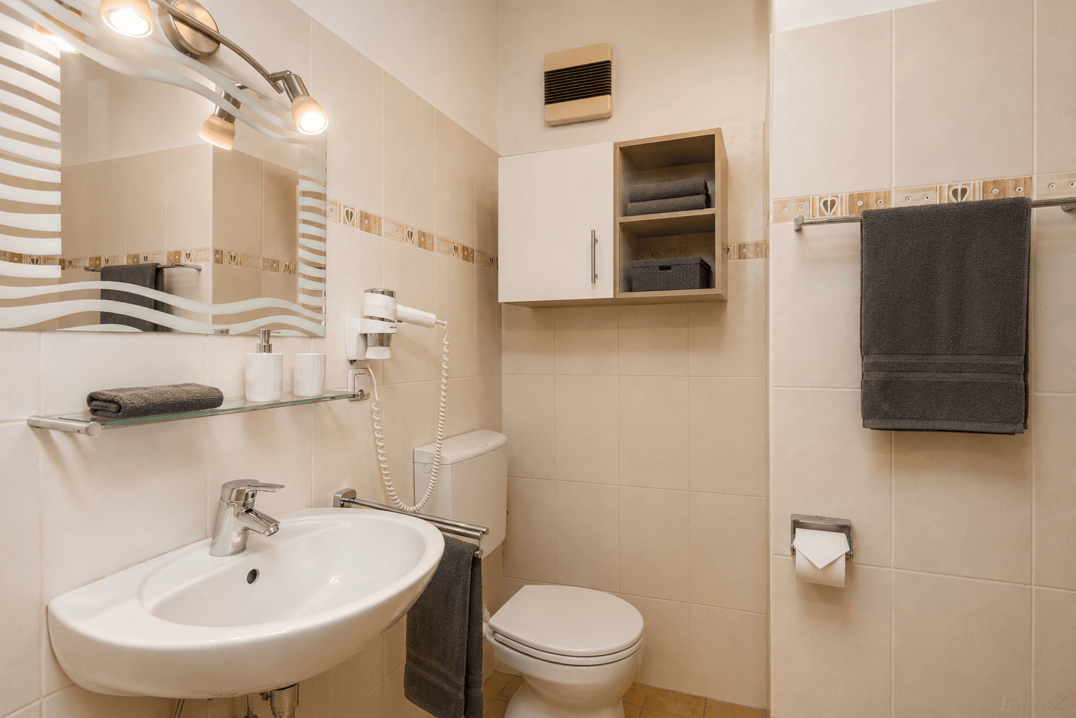 Modernes Badezimmer mit Waschbecken, Toilette, Spiegel und beigefarbenen Fliesen.