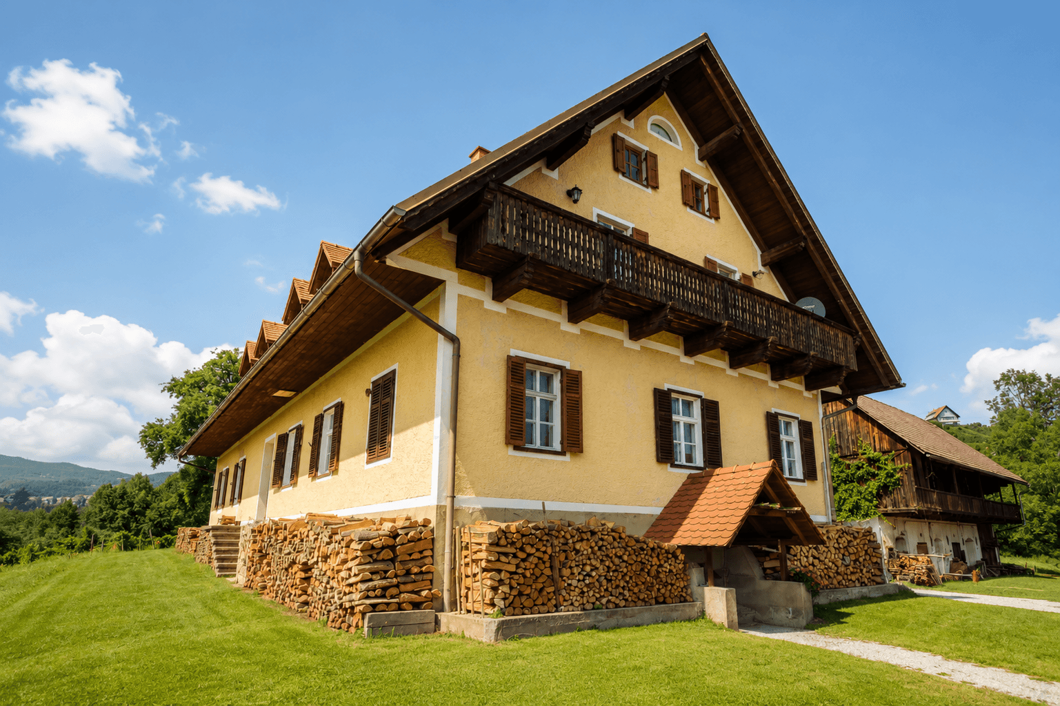 Traditionelles Landhaus mit gelber Fassade, Holzbalkonen und gestapeltem Brennholz.