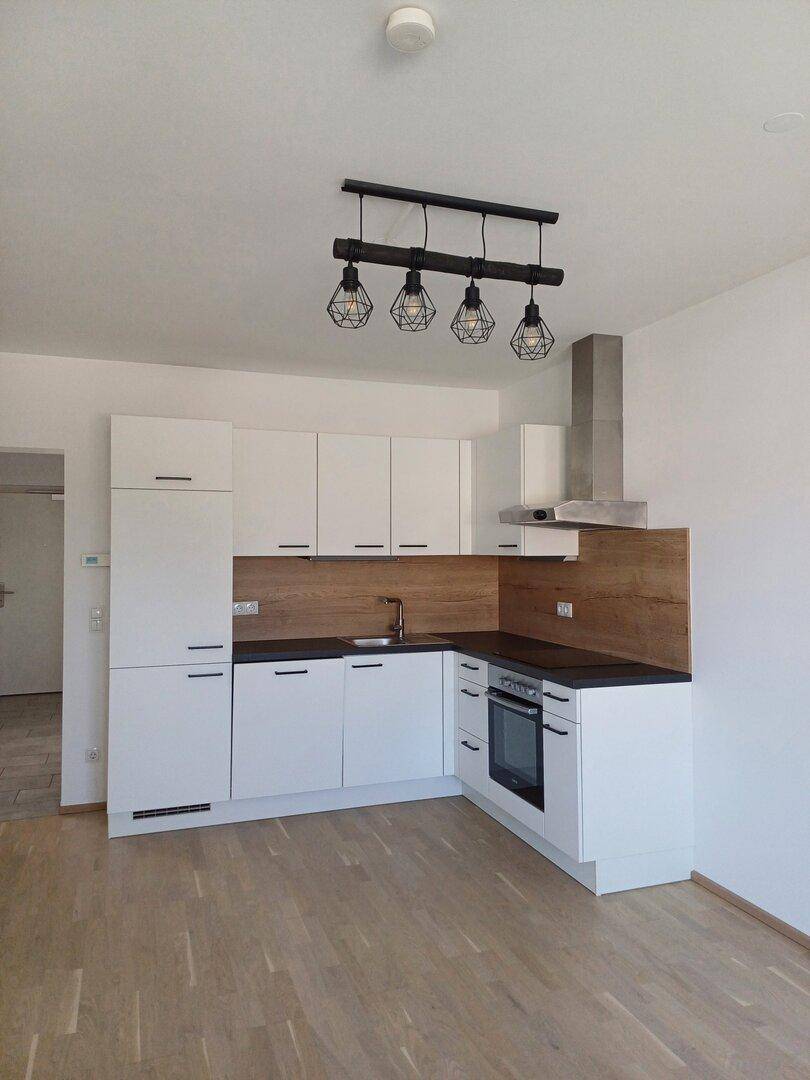 Leere Küche mit weißen Einbauschränken, Holzakzenten und modernen Geräten, bereit zur ersten Nutzung.