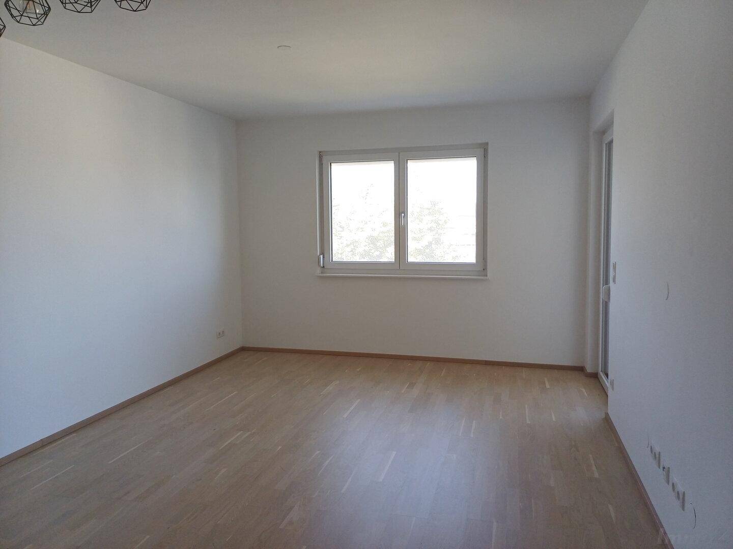 Heller, leerer Raum mit Holzboden, großem Fenster und Zugang zu einem Außenbereich, bietet viel Potenzial.