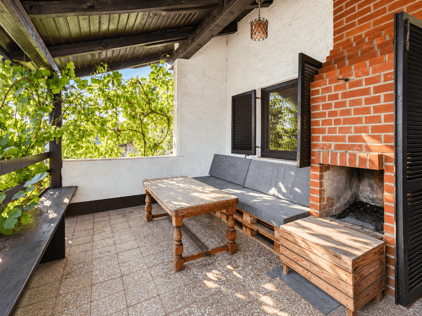 Gemütliche überdachte Terrasse mit gemauertem Grill, Palettenmöbeln und Blick ins Grüne.