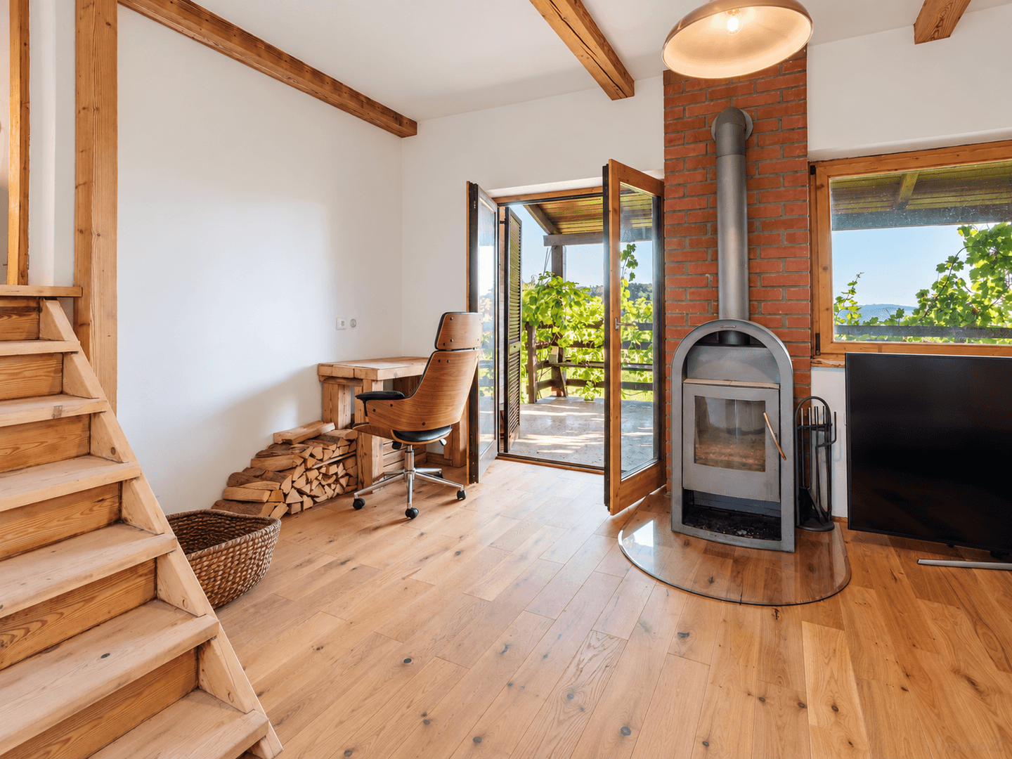Heller Wohnbereich mit Holzboden, freiliegenden Balken, Kaminofen und Zugang zur Terrasse.