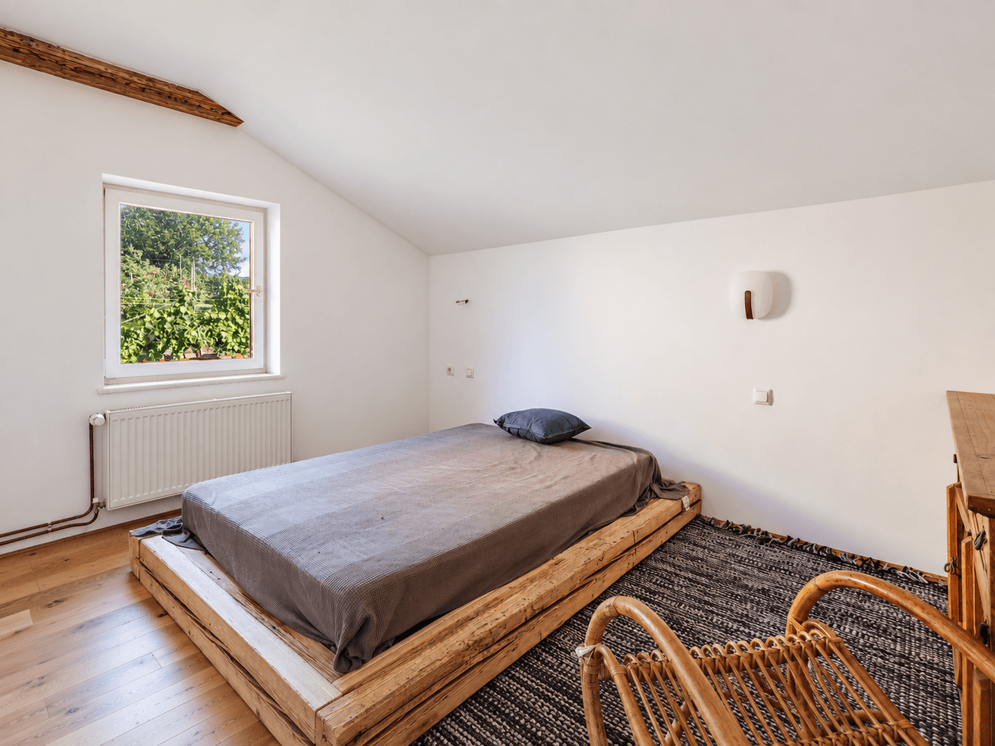 Schlafzimmer mit Holzboden, einem niedrigen Holzbett und einem Fenster mit Blick ins Grüne.