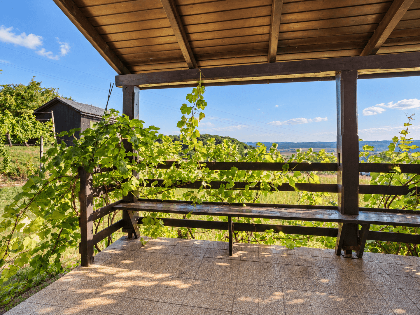 Überdachte Terrasse mit Holzbänken und einem malerischen Blick auf die umliegenden Weinberge.