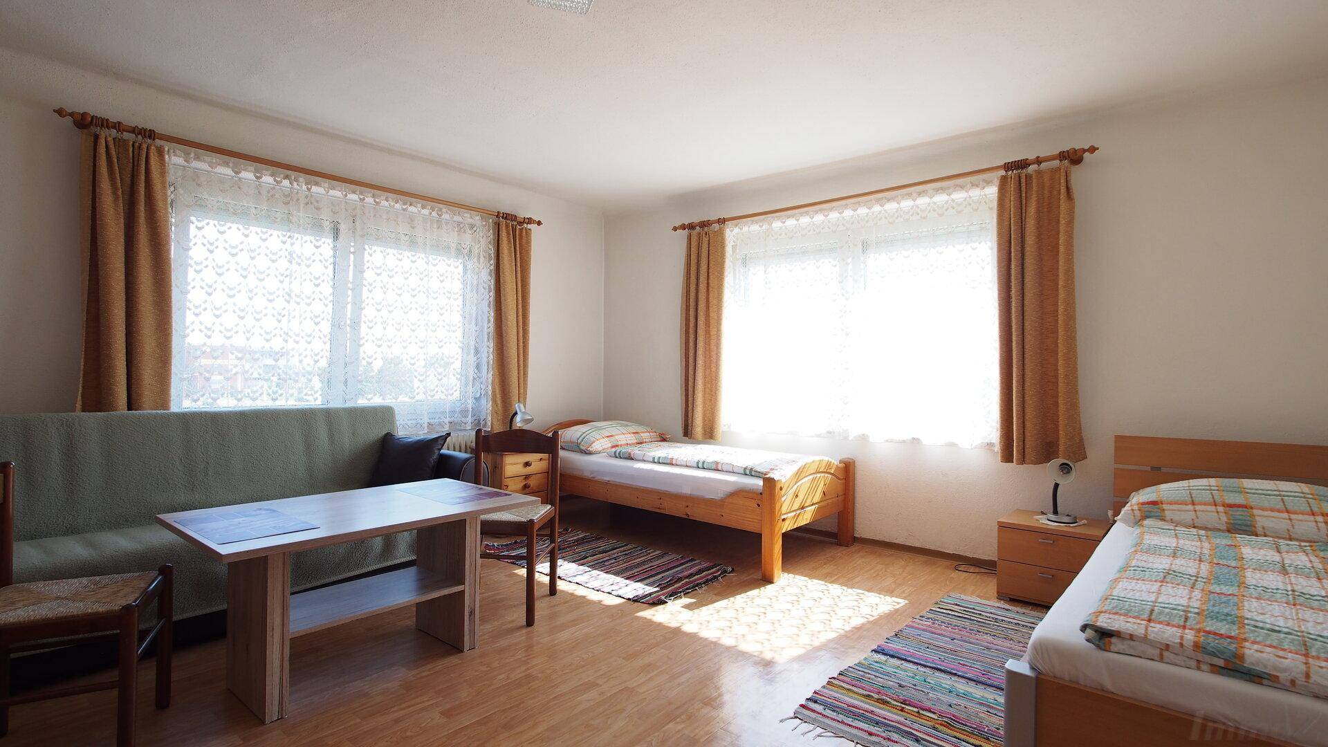 Helles Schlafzimmer mit zwei Einzelbetten, einem Sofa und einem Tisch, ausgestattet mit Holzmöbeln.