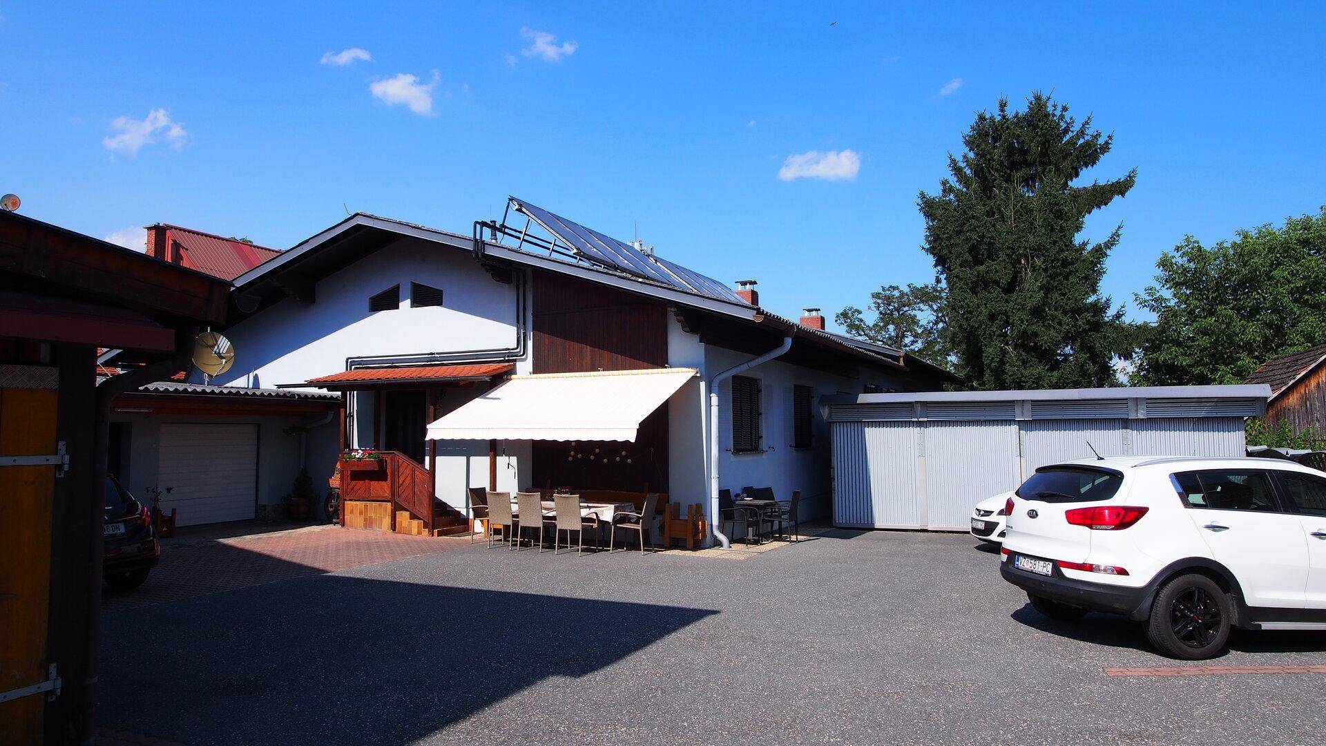 Gebäude mit Photovoltaikanlage auf dem Dach, umgeben von einem Parkplatz und einem weißen Auto.