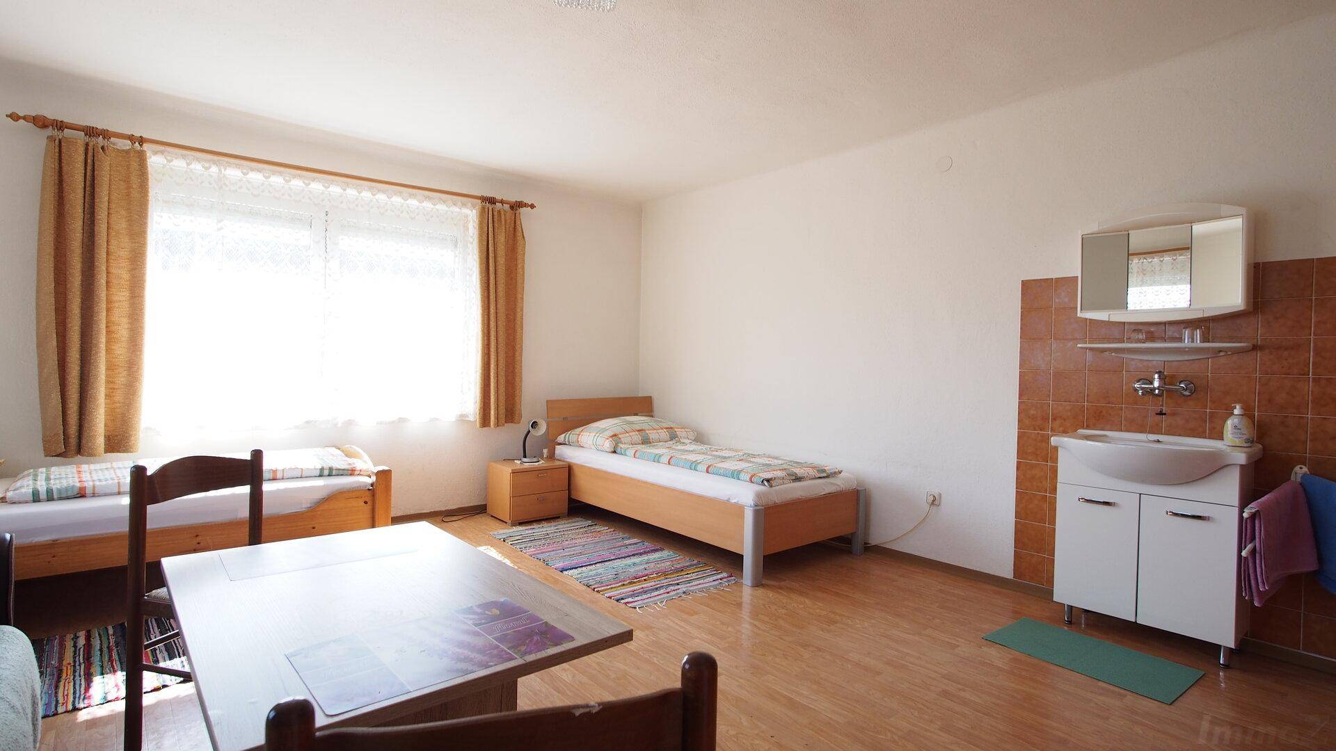 Einfaches Schlafzimmer mit zwei Betten, Holzboden und einem Waschbeckenbereich an der Wand.