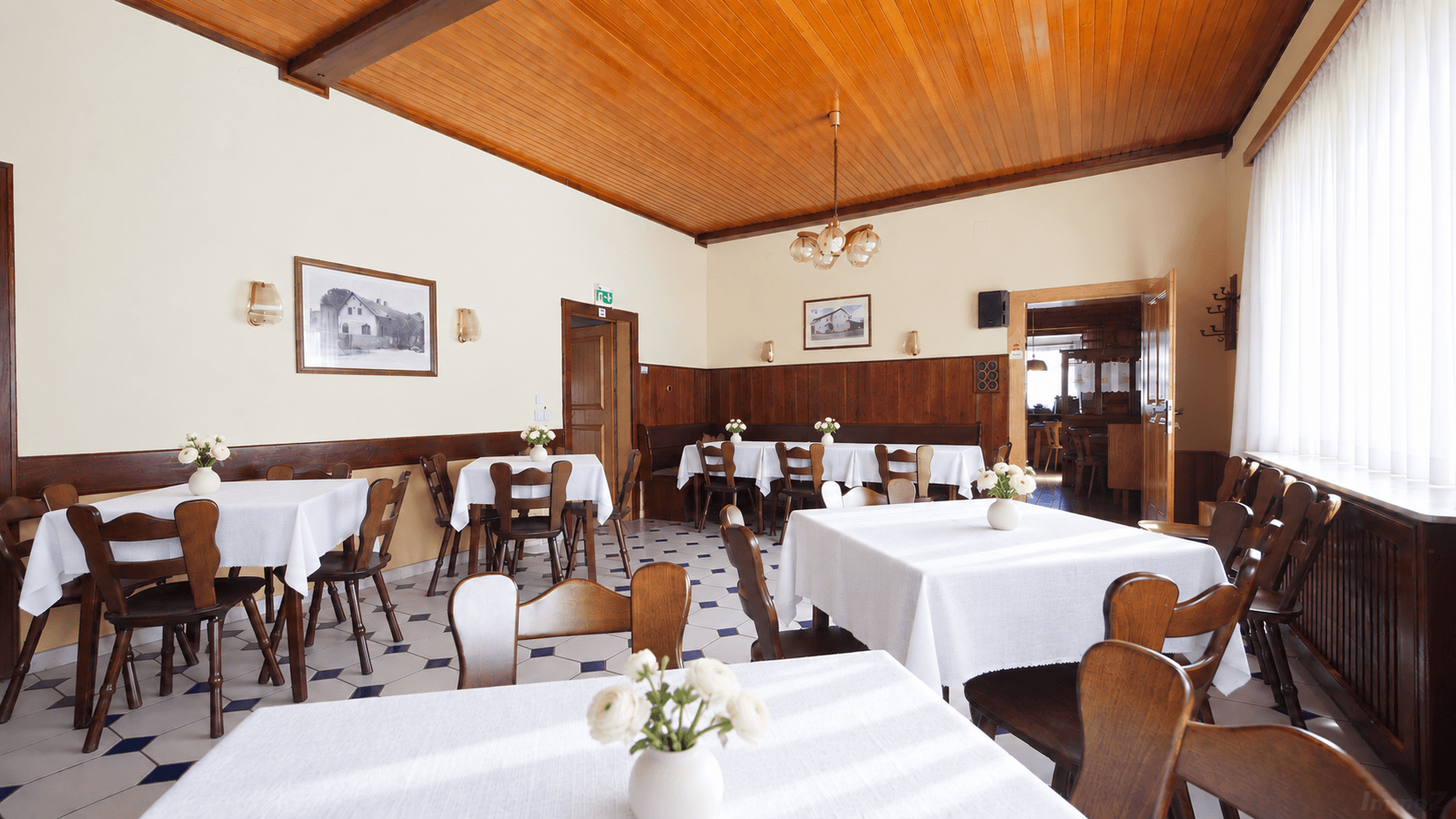 Geräumiger Speisesaal mit Holztäfelung, Holzbalkendecke und traditionellen Tischen mit weißen Tischdecken.