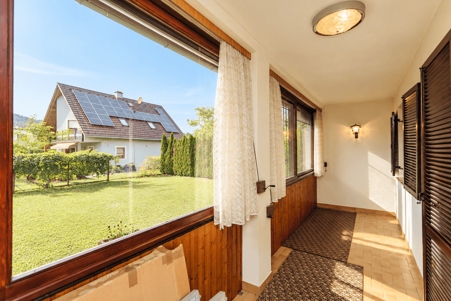Verglaste Loggia mit Holzelementen und weitem Blick auf den Garten und die Umgebung.