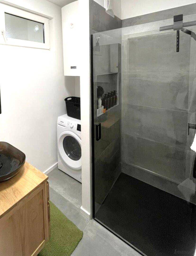 Modernes Badezimmer mit ebenerdiger Dusche, Waschmaschine und kleinem Fenster für natürliche Belüftung.
