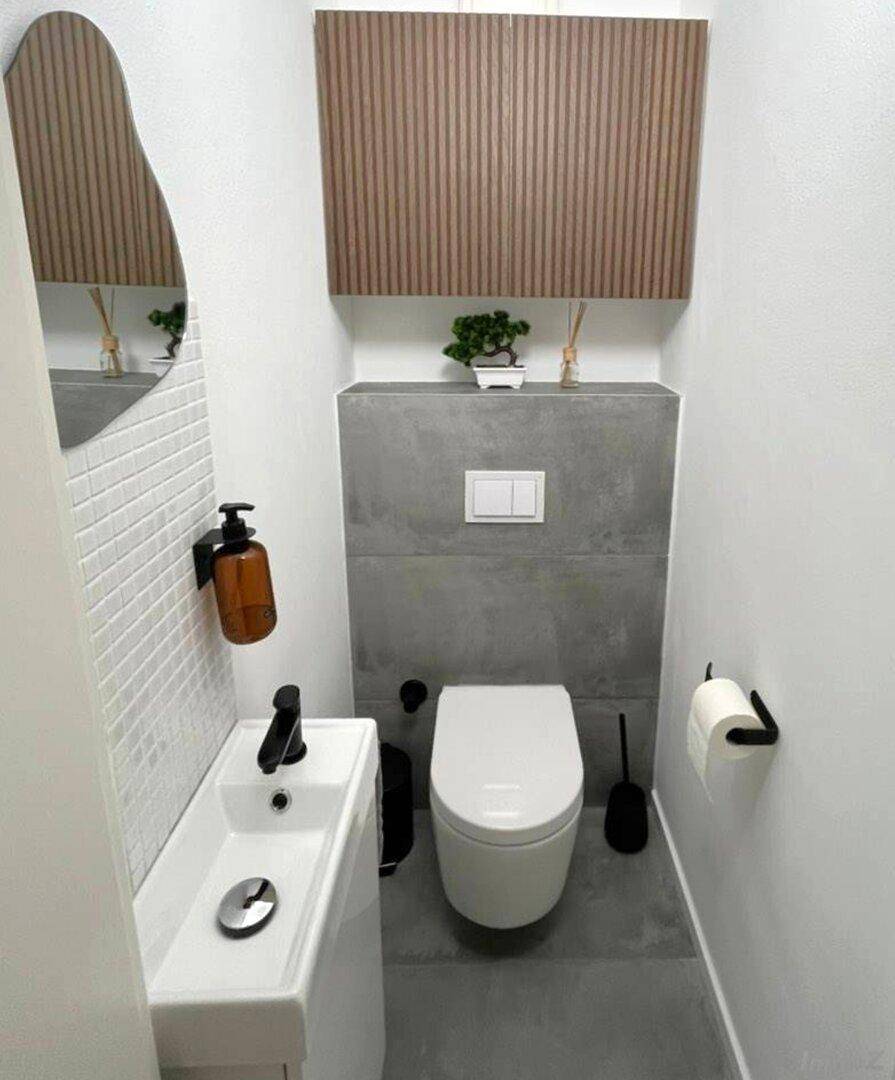 Modernes Gäste-WC mit wandhängender Toilette, kleinem Waschbecken und stilvollen Holzdetails.